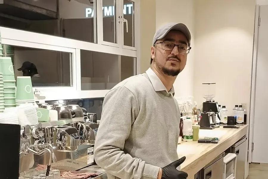 Ahmed Hussain at the bar of a café he helped set up, beside the espresso machine