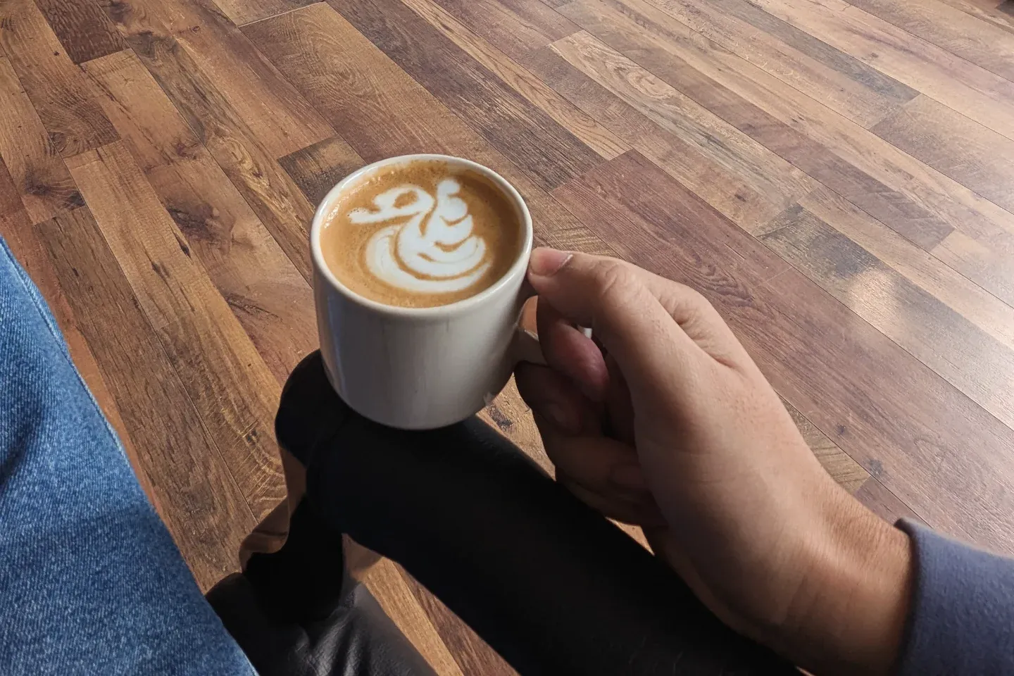A latte with rosetta art held over a wooden café floor